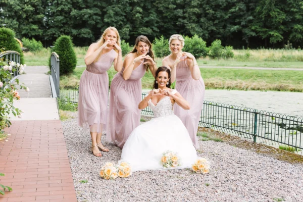 Braut und Brautjungfern mit Herzgesten im Park des Schloss Raesfeld bei einer Sommerhochzeit