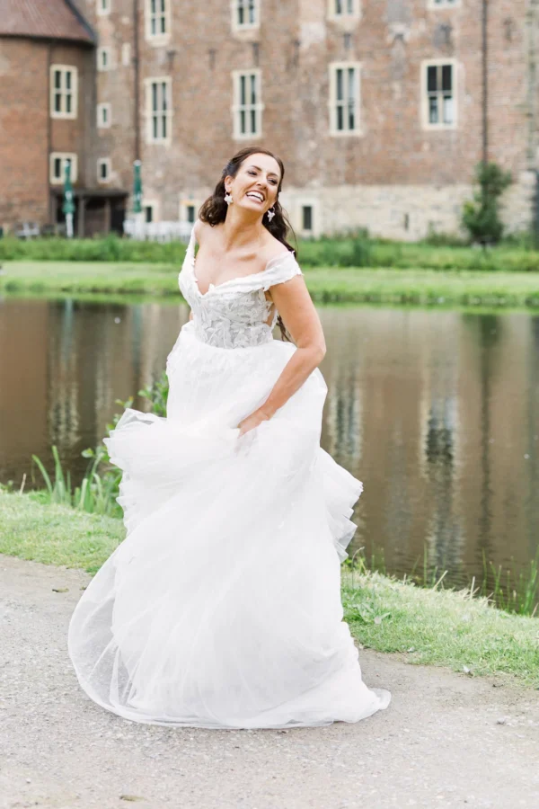 strahlende Braut tanzt im Hochzeitskleid am Wasser bei Schloss Raesfeld