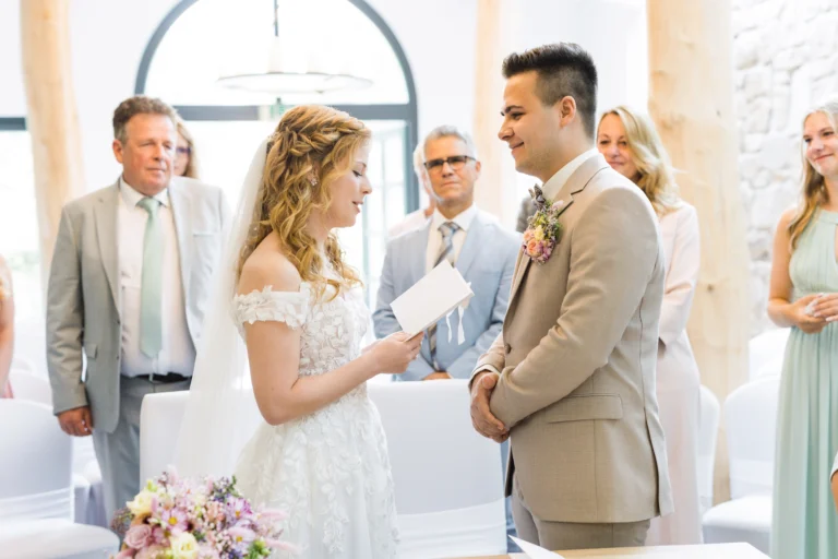 Braut im weißen Spitzenkleid liest ihrem Bräutigam beim Trauritual im Confideum Voshövel das Ehegelübde vor.