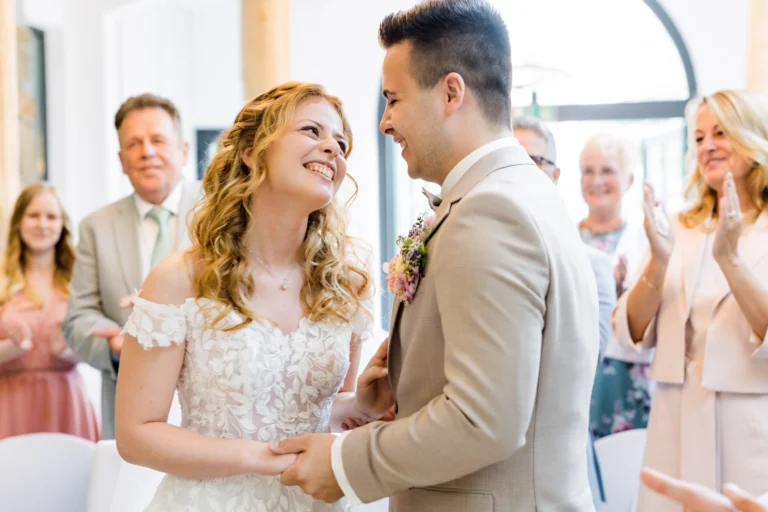 Braut und Bräutigam lächeln sich während ihrer standesamtlichen Zeremonie im Landhotel Voshövel Hochzeit an – ein emotionaler Moment vor den jubelnden Gästen.