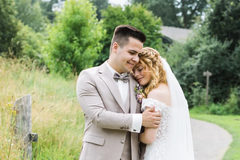 Braut und Bräutigam umarmen sich innig inmitten einer grünen Landschaft bei ihrer Voshövel Hochzeit. Die Braut schließt die Augen und lächelt.