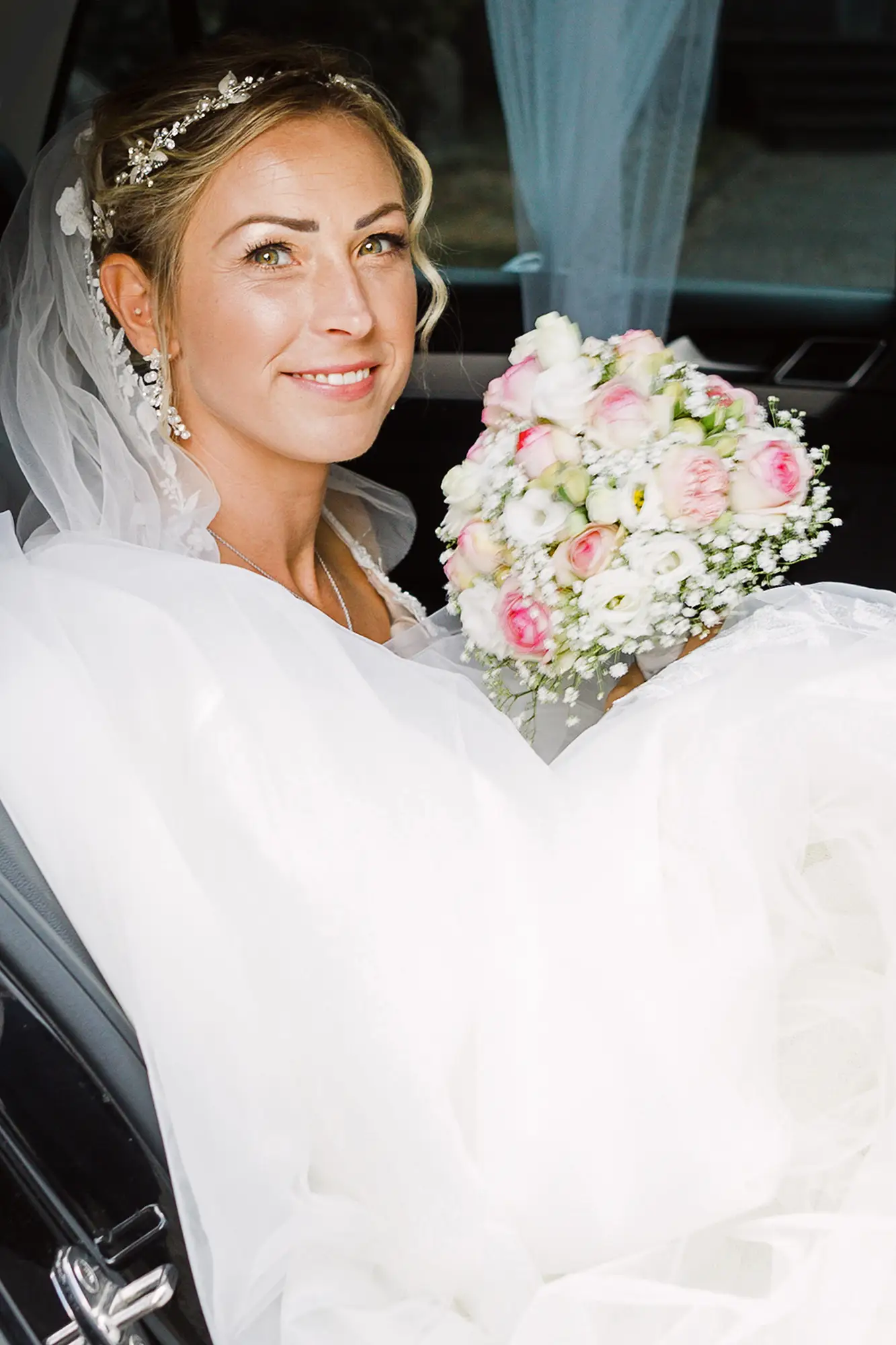 Eine glückliche Braut mit Brautstrauß im Hochzeitsauto – aufgenommen von einem Hochzeitsfotograf in Düsseldorf, Preis auf Anfrage.