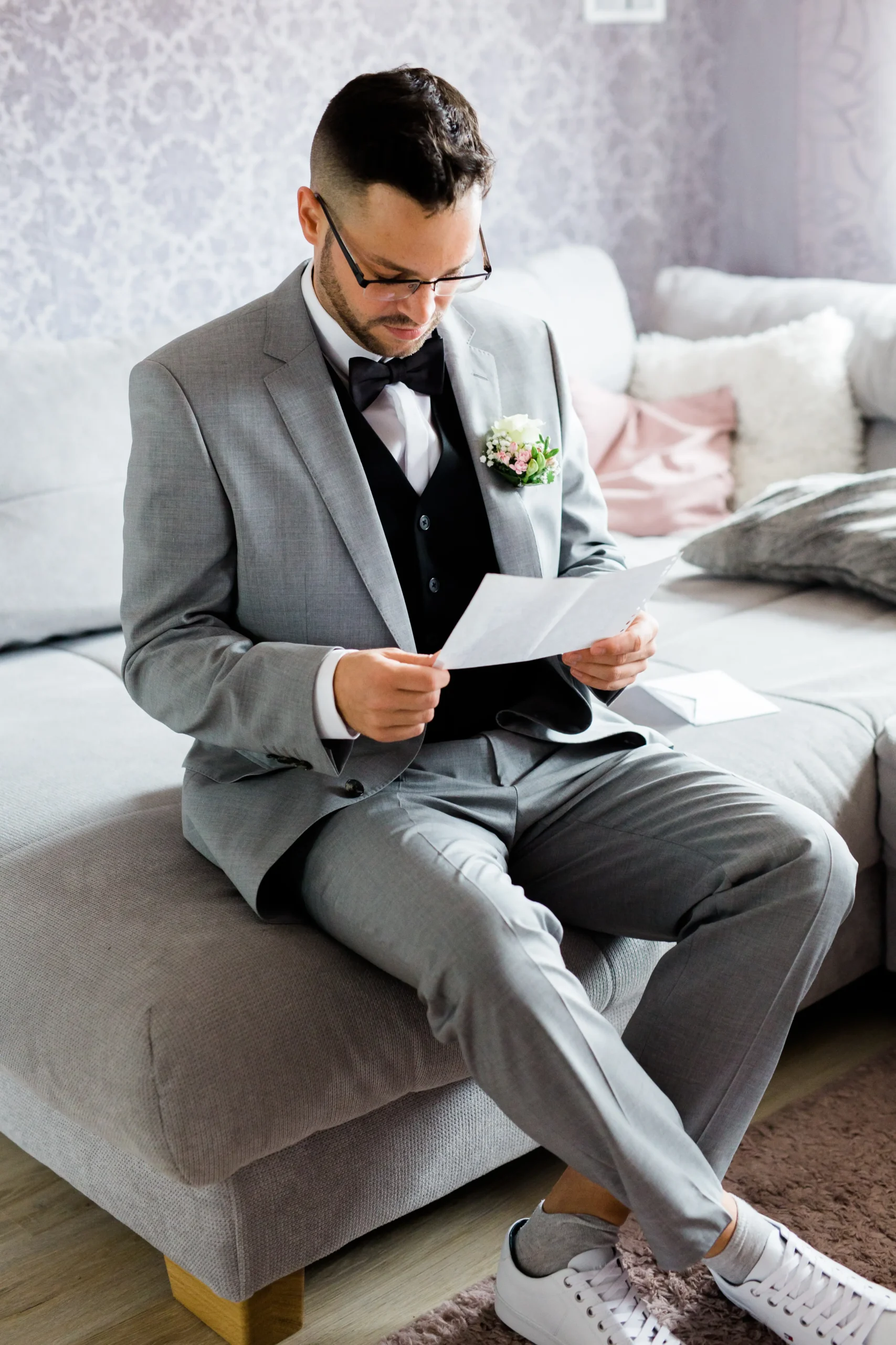 Der Bräutigam sitzt auf dem Sofa und liest einen liebevollen Brief von der Braut – emotionales Getting Ready vor der Trauung.