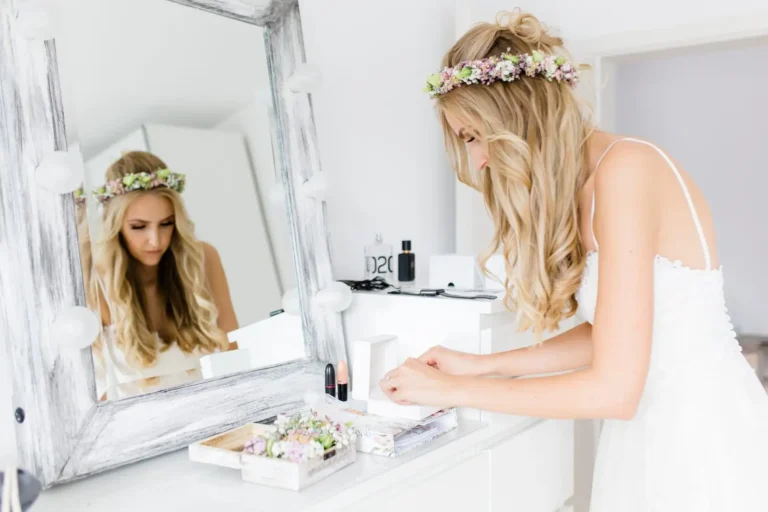 Eine Braut mit Blumenkranz stylt sich am Schminktisch und schaut in den Spiegel – romantisches Getting Ready vor der Hochzeit.